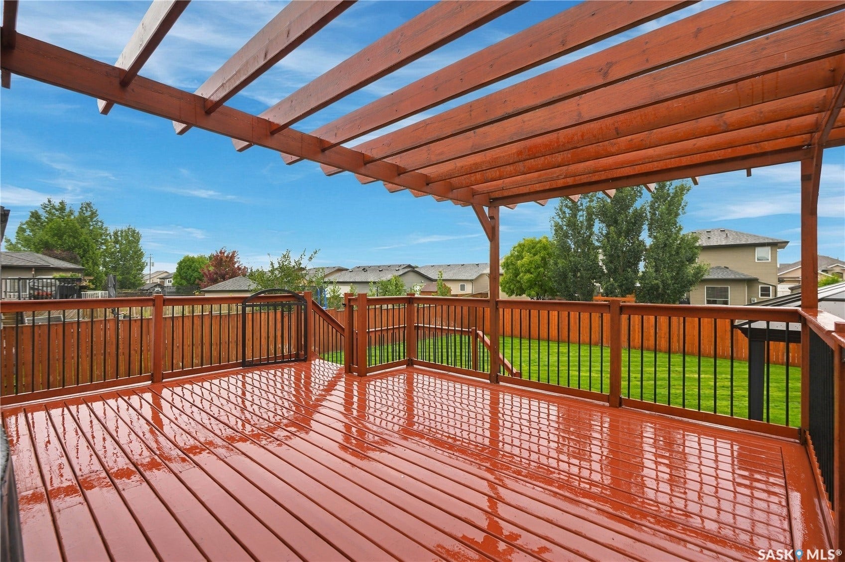 Expansive wood deck with a pergola, dark iron railings, and a privacy fence