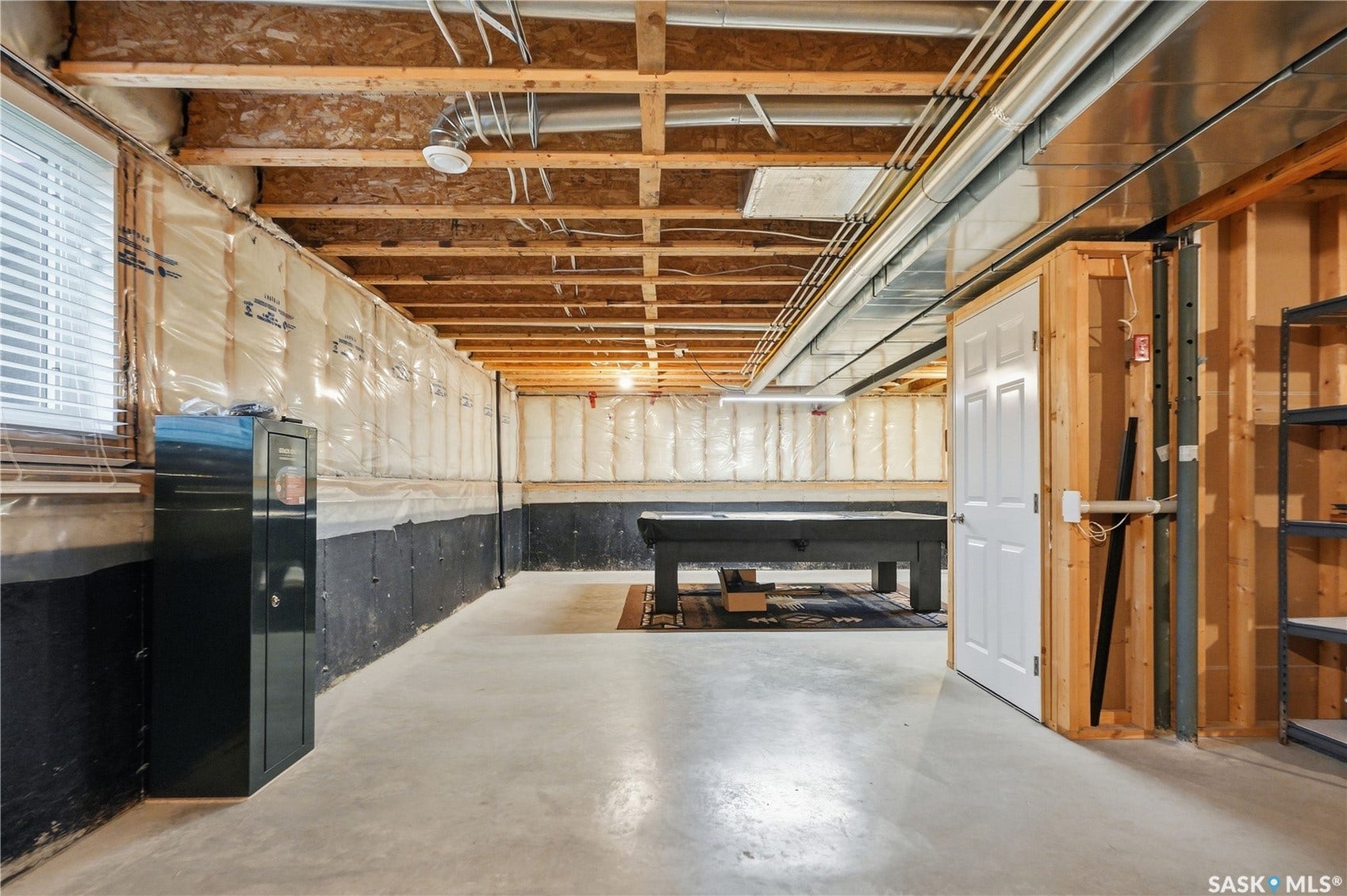 Unfinished basement featuring exposed wood joists, concrete flooring, and a framed utility room with a white door