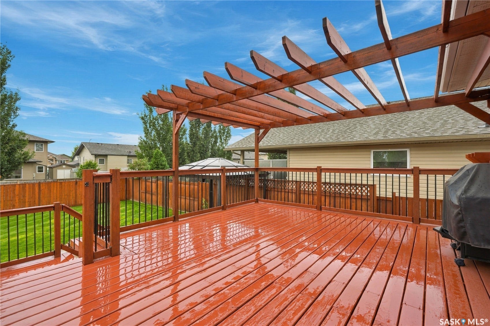 Expansive wooden deck featuring a pergola, wood railing with black balusters, and a gate providing access to the yard