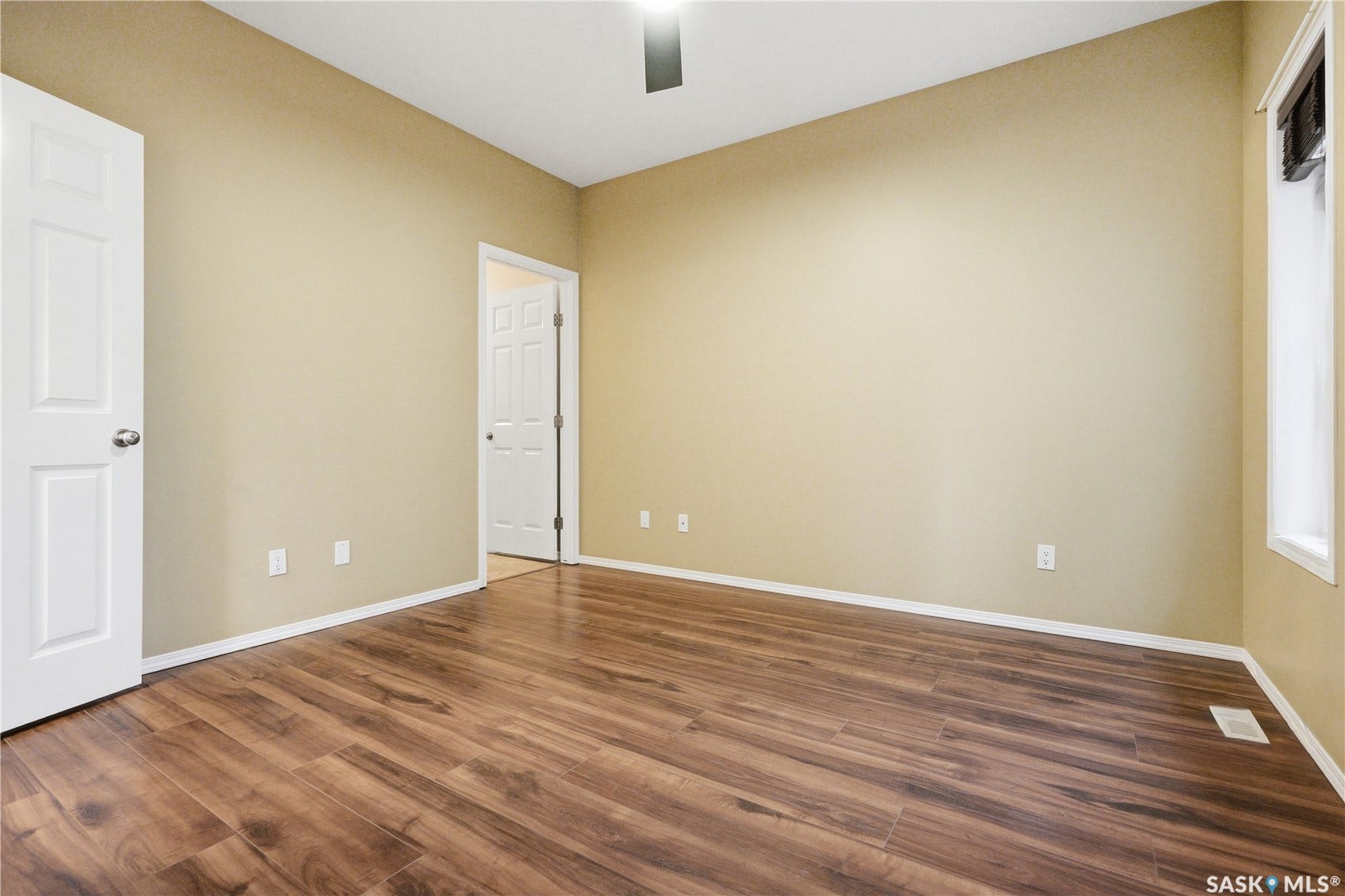 Wood-finish flooring, light-toned walls, ceiling fan, white trim, and a prominent window