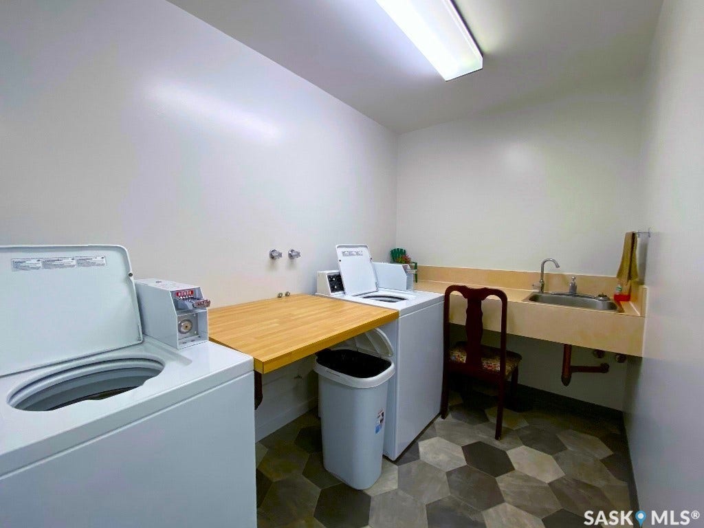 Laundry area featuring two washing machines, a utility sink with a faucet, a wood-finish countertop, and hexagonal floor tiling