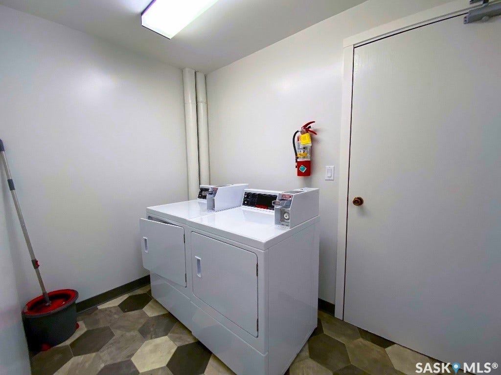 Commercial-grade washer and dryer units, hexagonal floor tiles, and a fluorescent ceiling light fixture