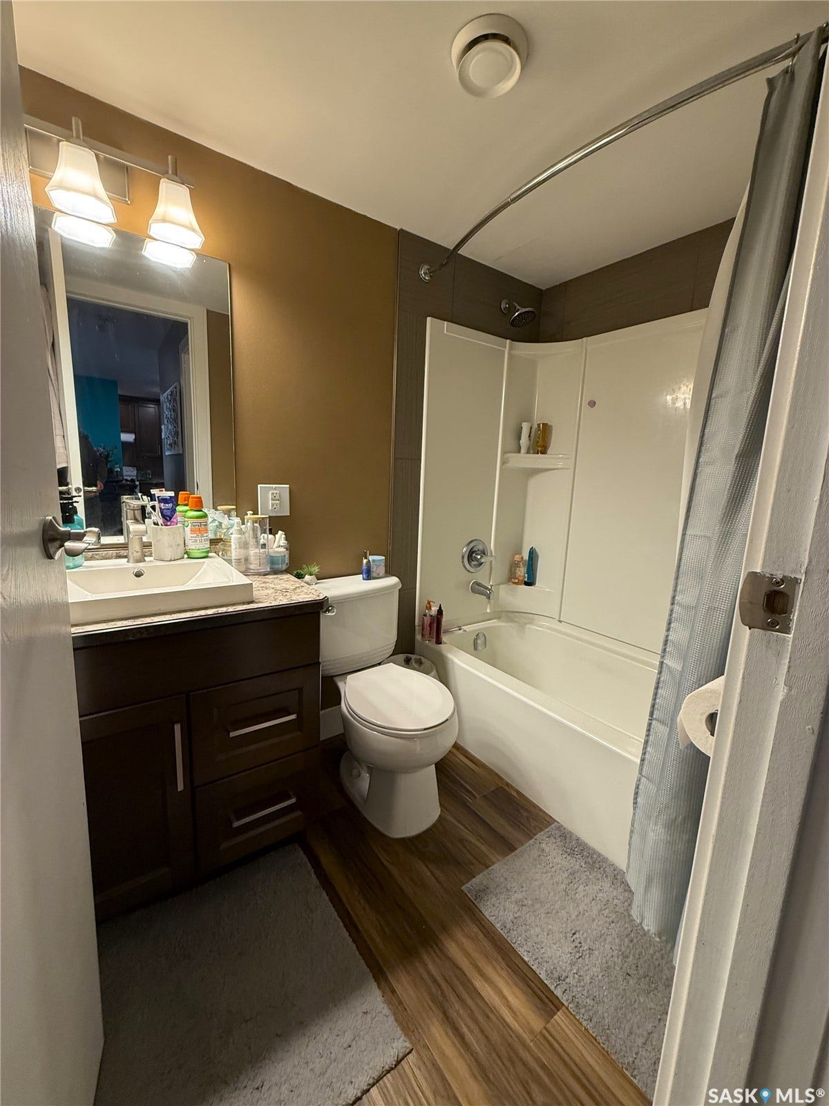 Dark wood-finish vanity with a rectangular sink, a shower/tub combination, and wood-finish flooring
