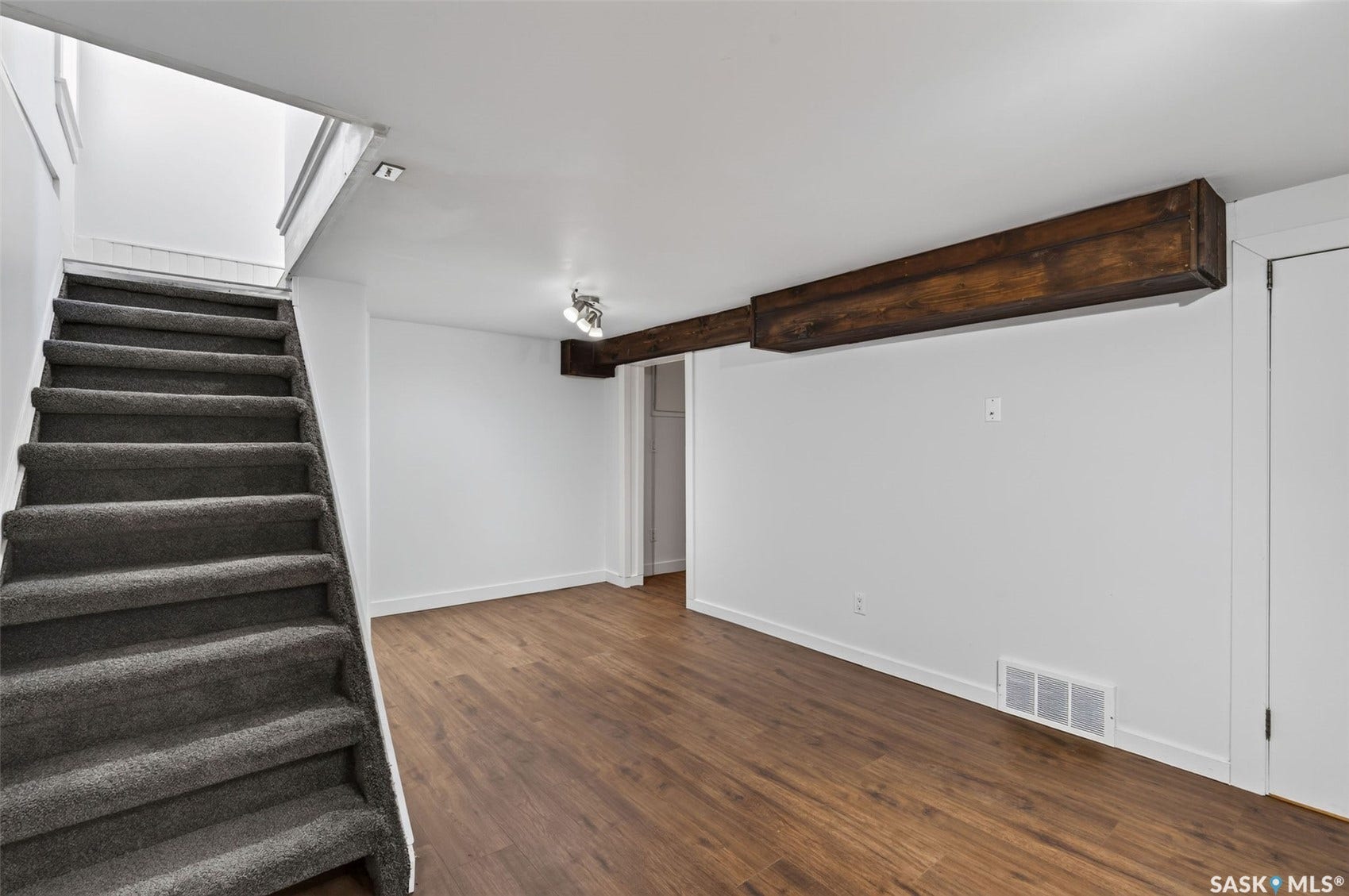 Wood-finish flooring, white walls, exposed wood beams, and a carpeted staircase