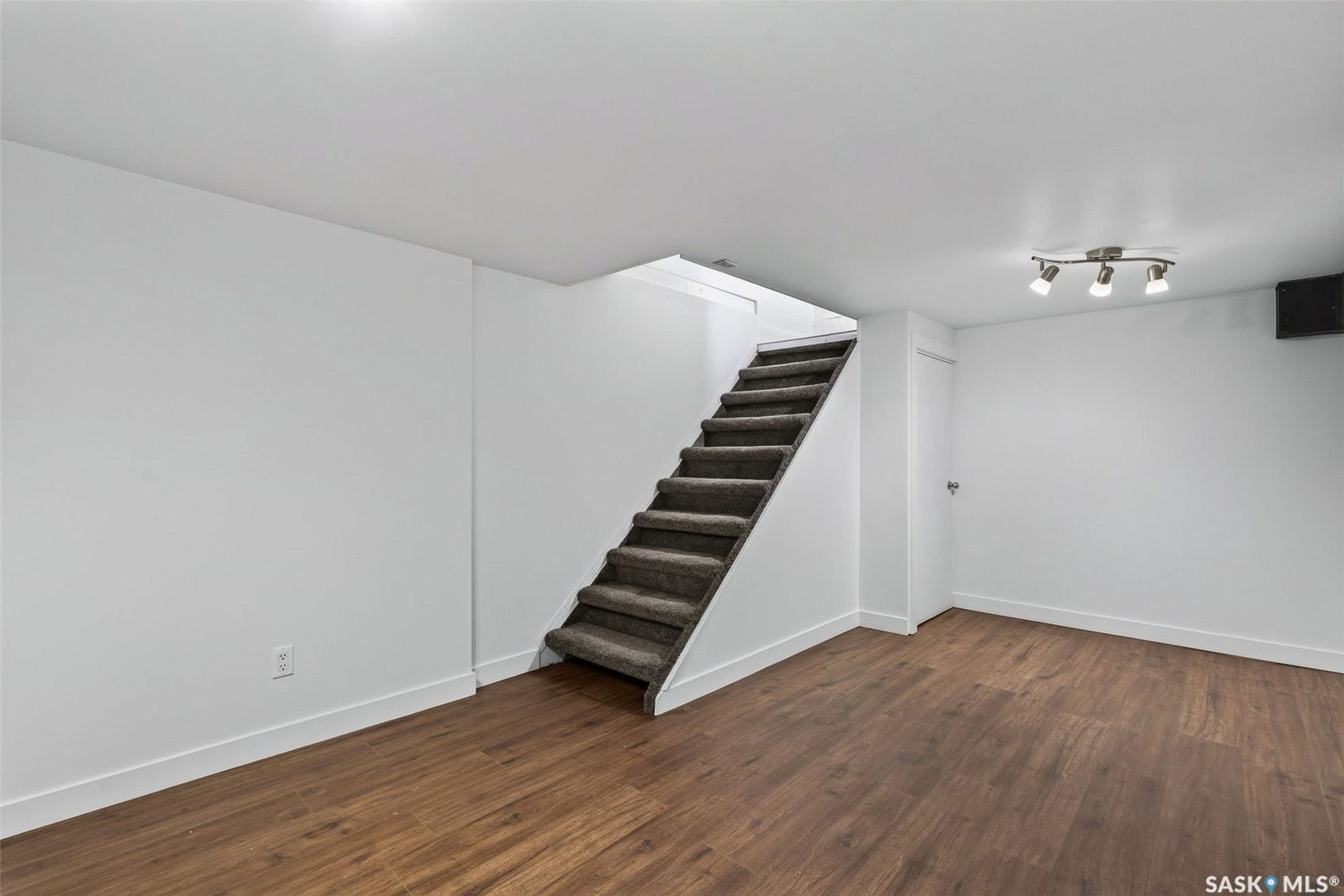 Carpeted staircase, wood-finish flooring, white walls, track lighting fixture, white trim
