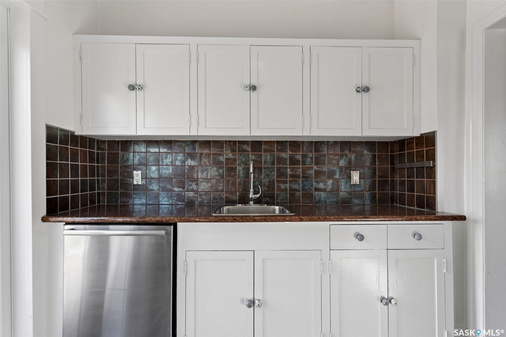 White cabinetry, dark square tile backsplash, stainless steel sink, stainless steel appliance, and dark countertop