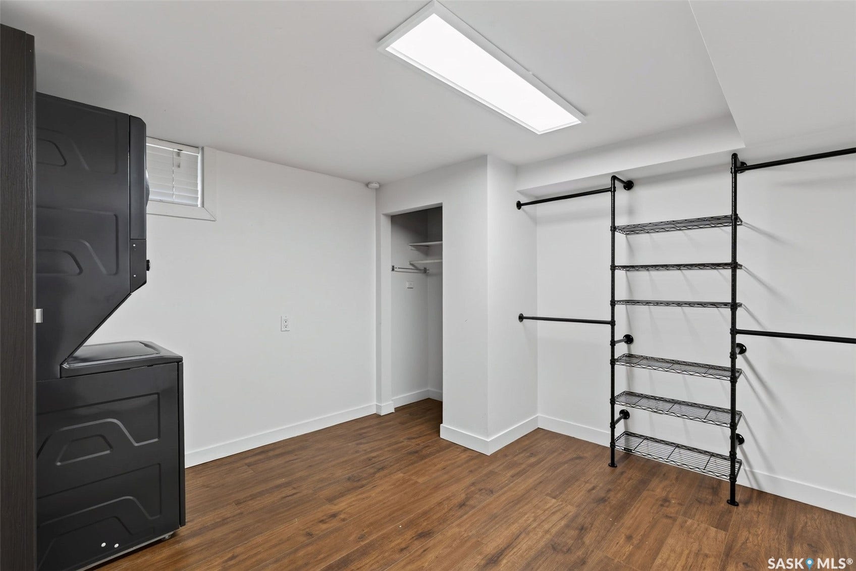Wood-finish flooring, white walls, built-in shelving, built-in clothing rods, and a rectangular ceiling light fixture