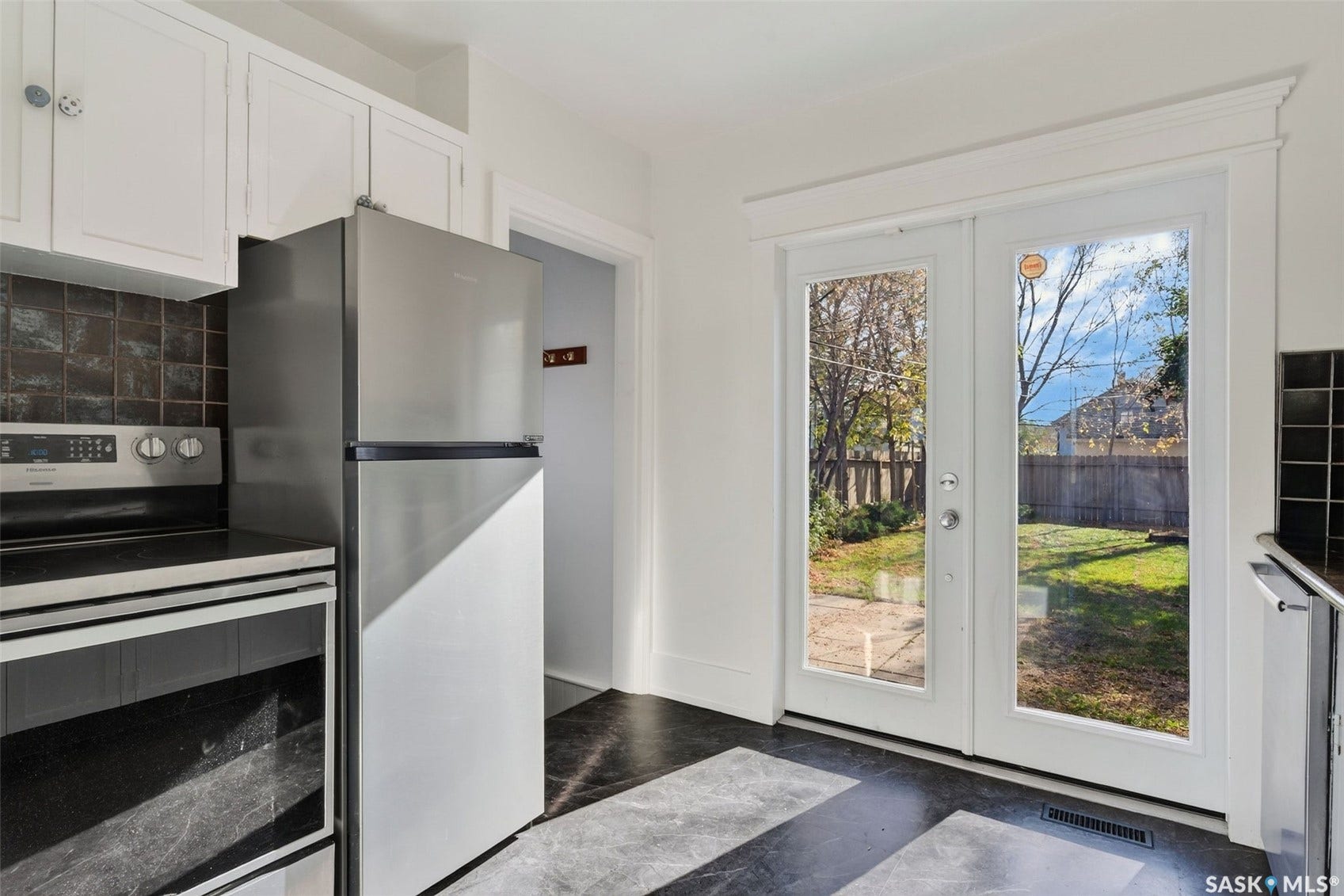 Stainless steel appliances, white cabinetry, dark tile backsplash, dark flooring, and glass-paneled double doors