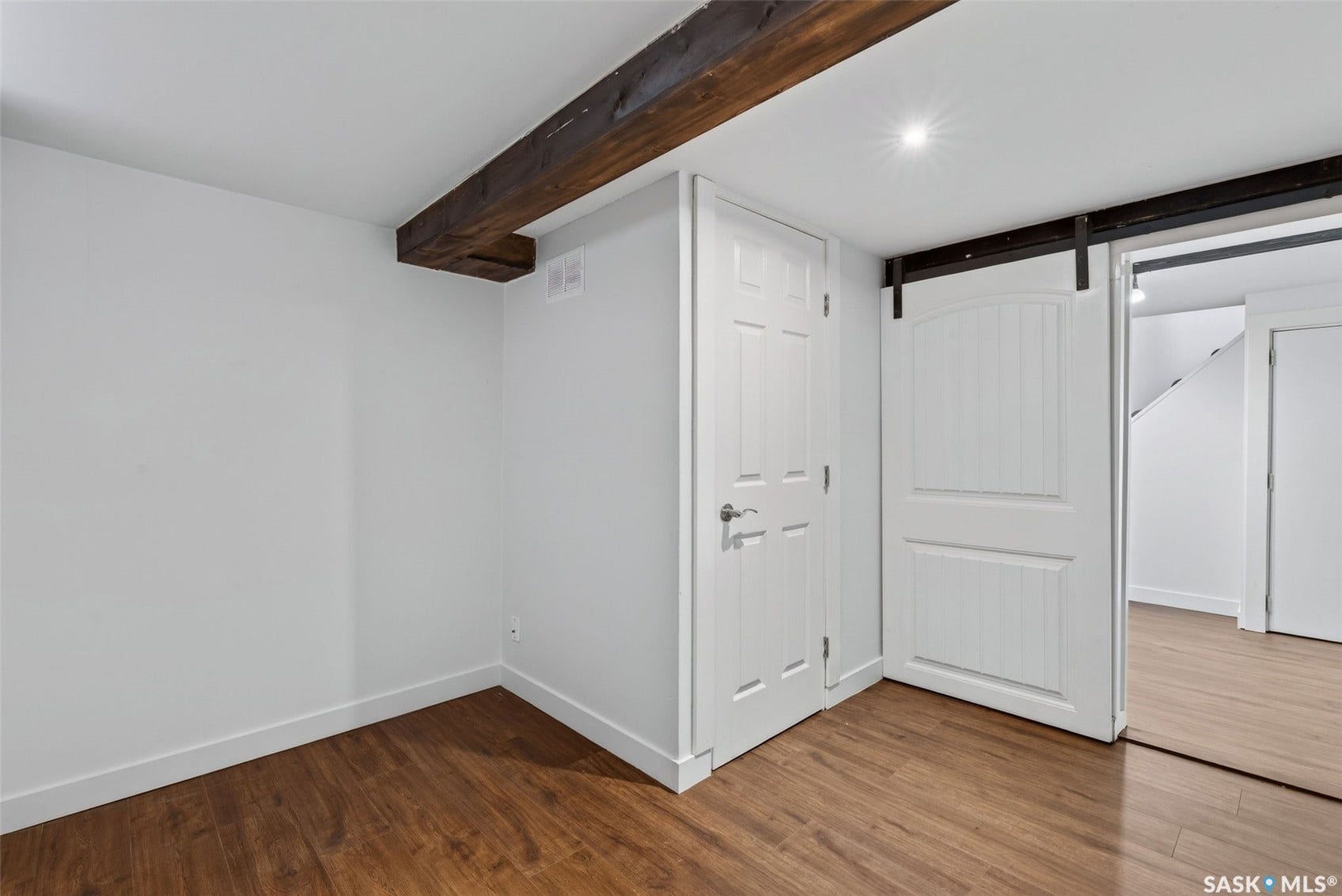 Wood-finish flooring, exposed ceiling beam, recessed lighting, white interior doors, and a sliding barn door