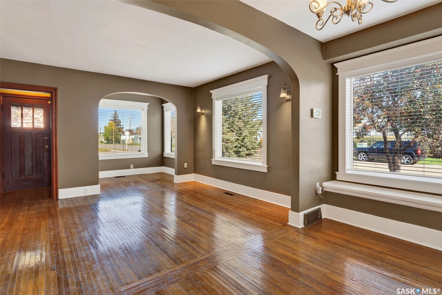 Hardwood flooring, arched doorways, multiple windows, decorative wall sconces, and a detailed wood entry door