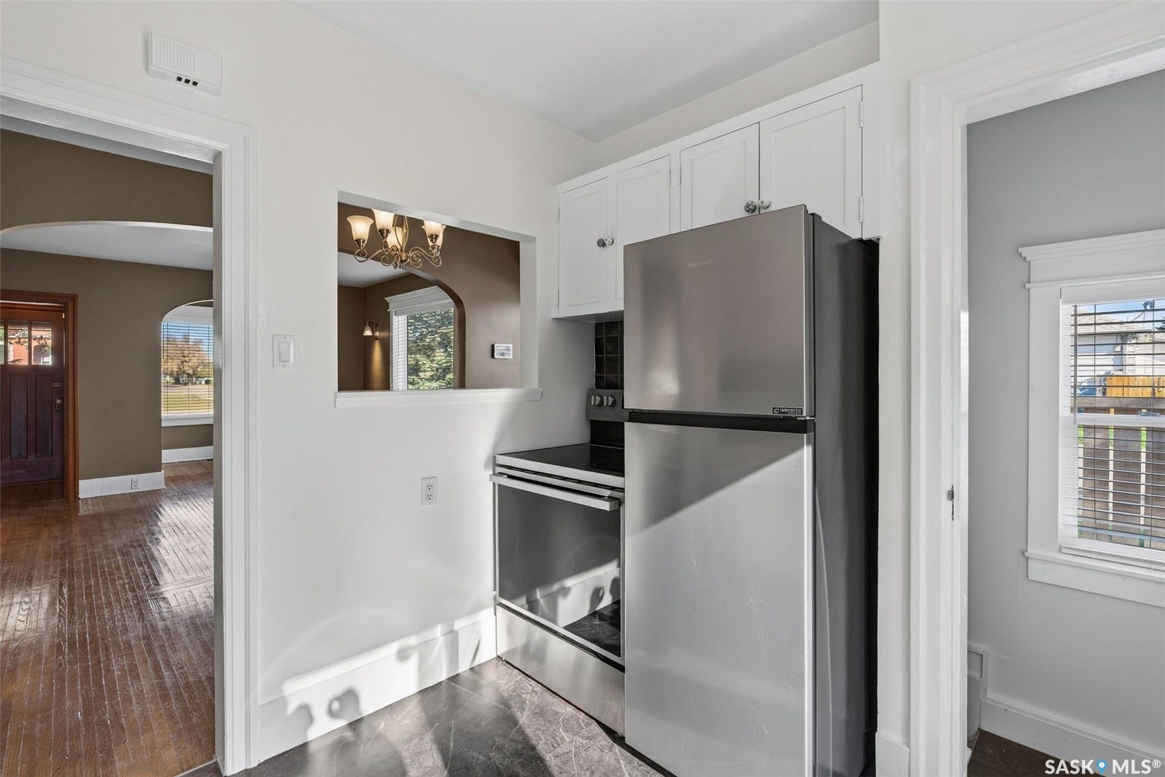 Kitchen featuring stainless steel appliances, white cabinetry, dark flooring, and a pass-through opening
