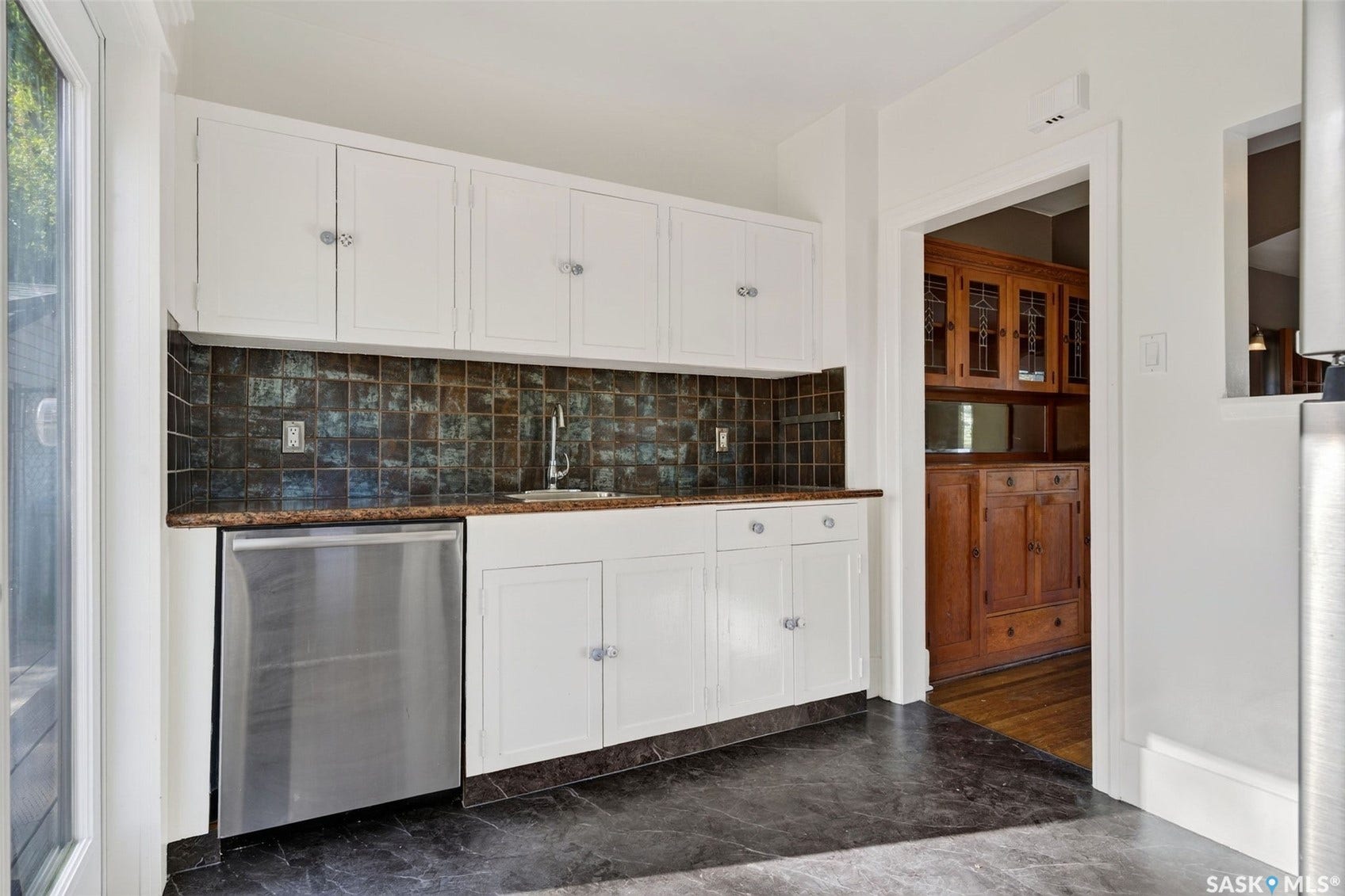 White cabinetry, dark square tile backsplash, stainless steel dishwasher, undermount sink, and dark floor tiling