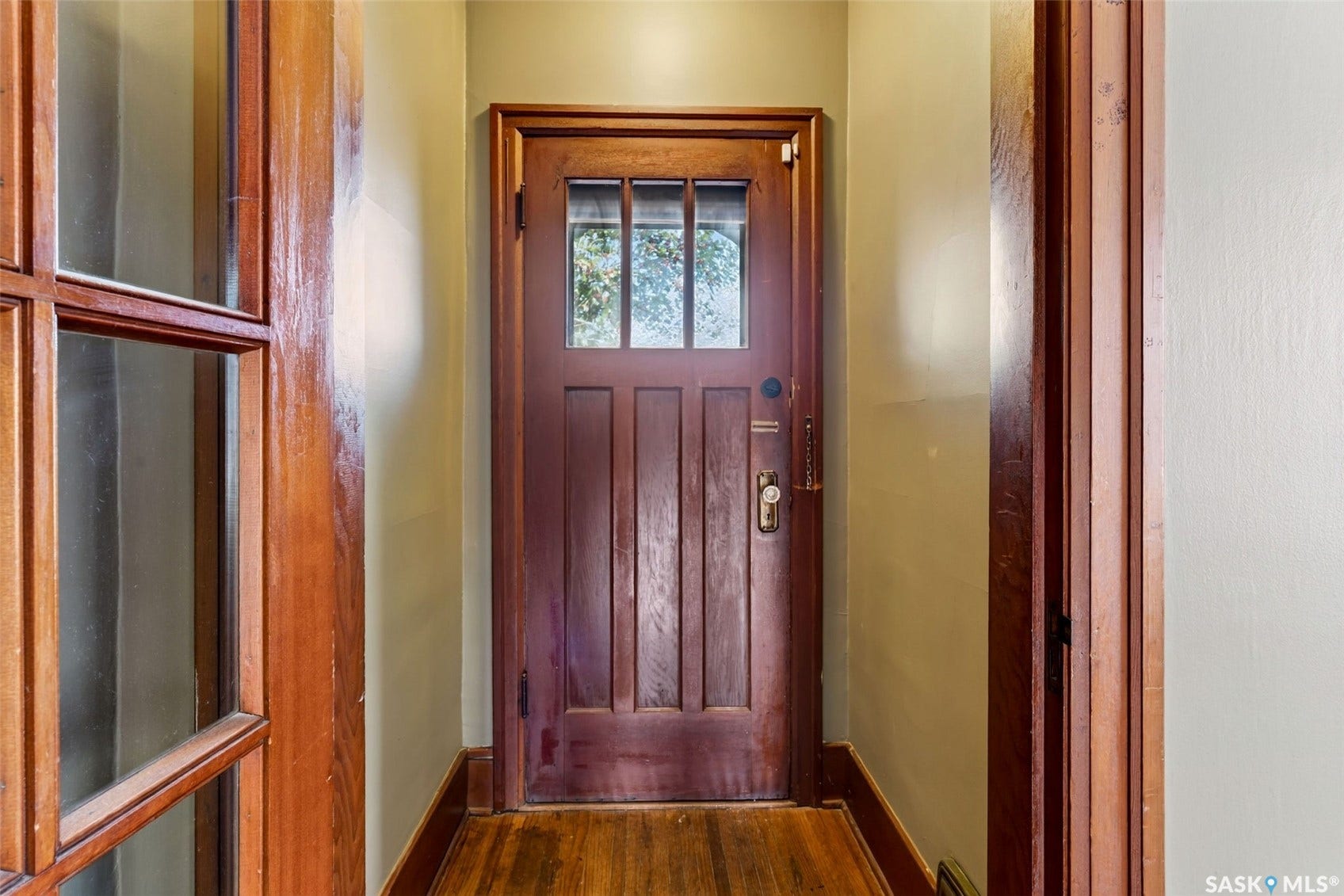Rich wood door with upper glass paneling, brass hardware, and wood-finish flooring