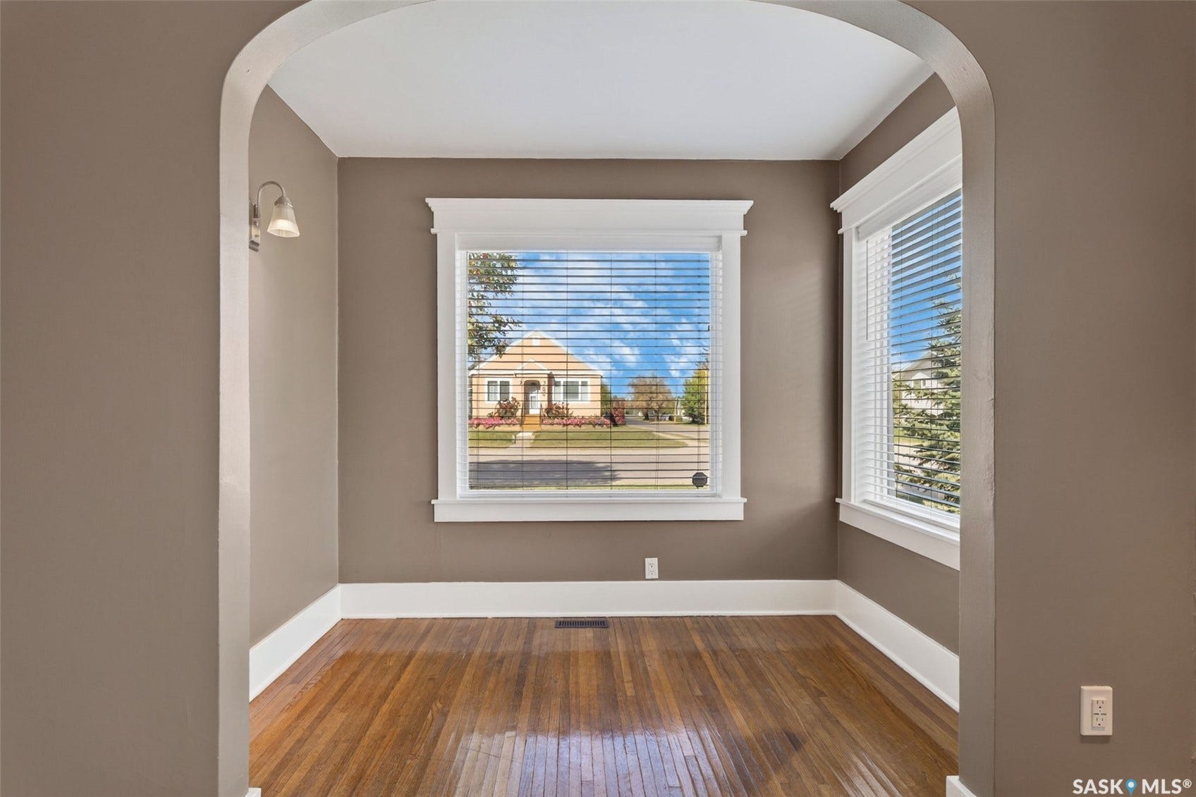 Archway entry framing a room with hardwood flooring, white trim details, and multiple windows