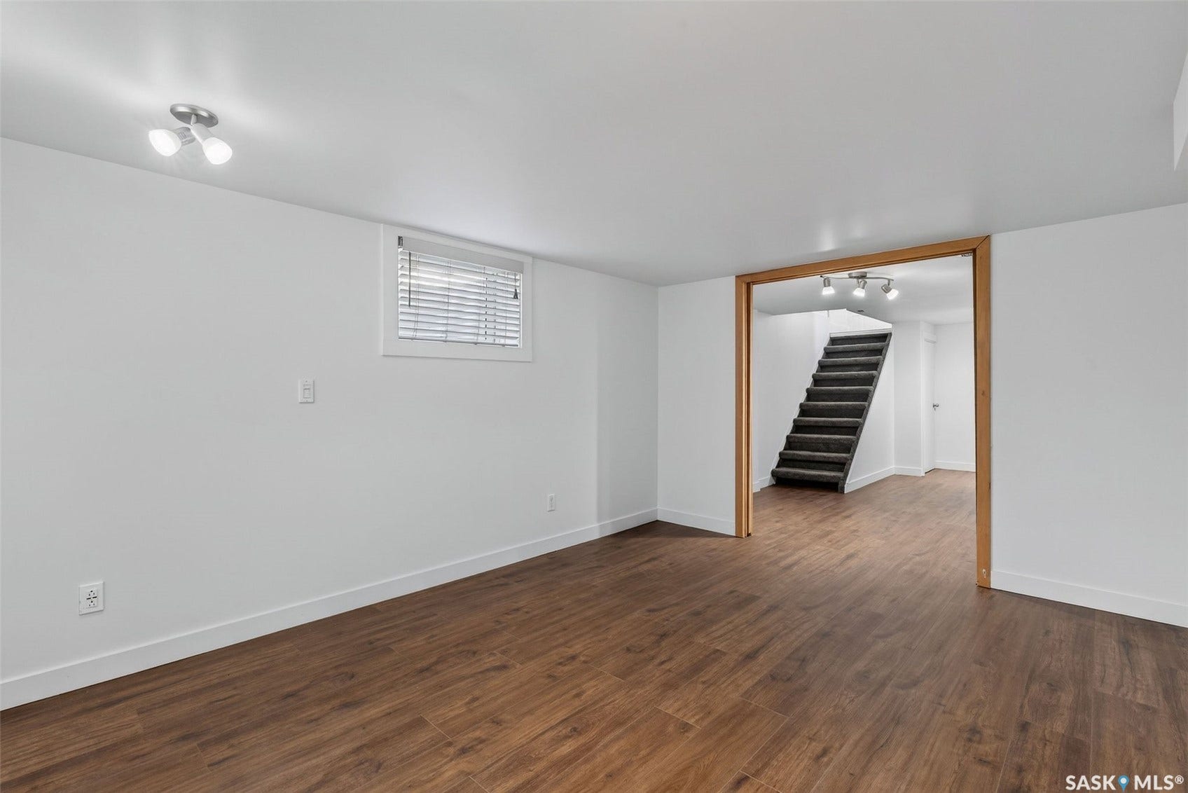 Spacious room featuring wood-finish flooring, white walls, and a recessed window with blinds