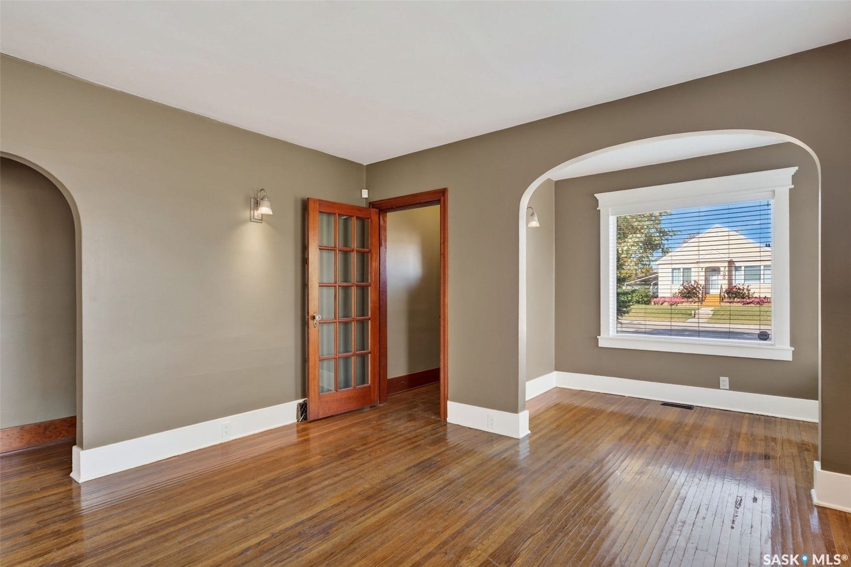 Hardwood flooring, arched doorways, white trim, wall sconces, and a paneled glass door