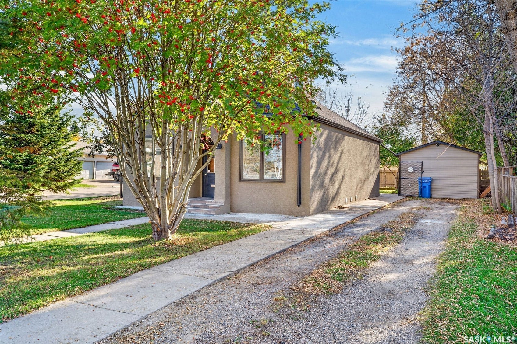 Stucco exterior residence with a side-facing gravel driveway, a separate concrete pathway, and a detached shed