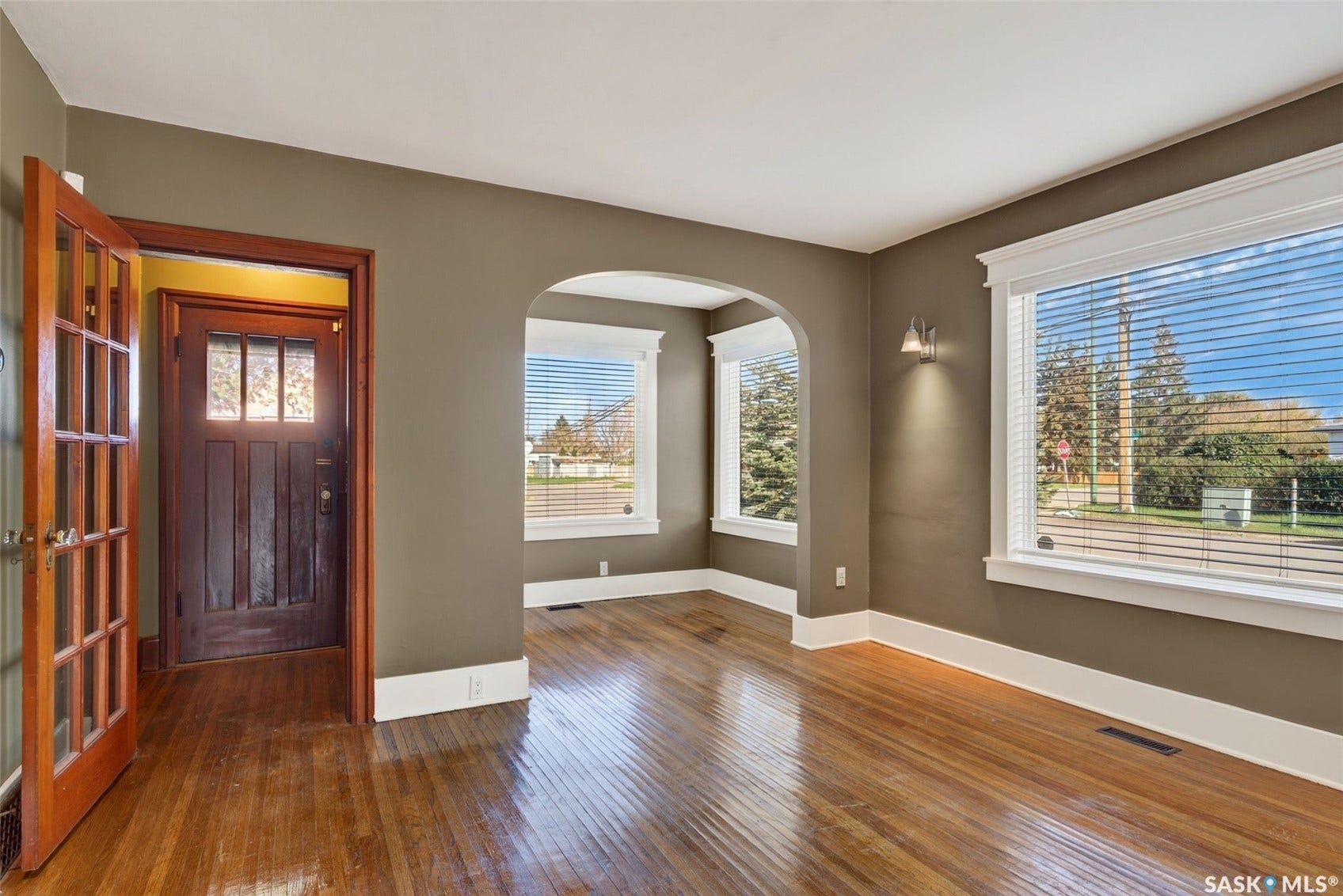 Hardwood flooring, arched doorway, sconce lighting, white trim, and a paneled entry door