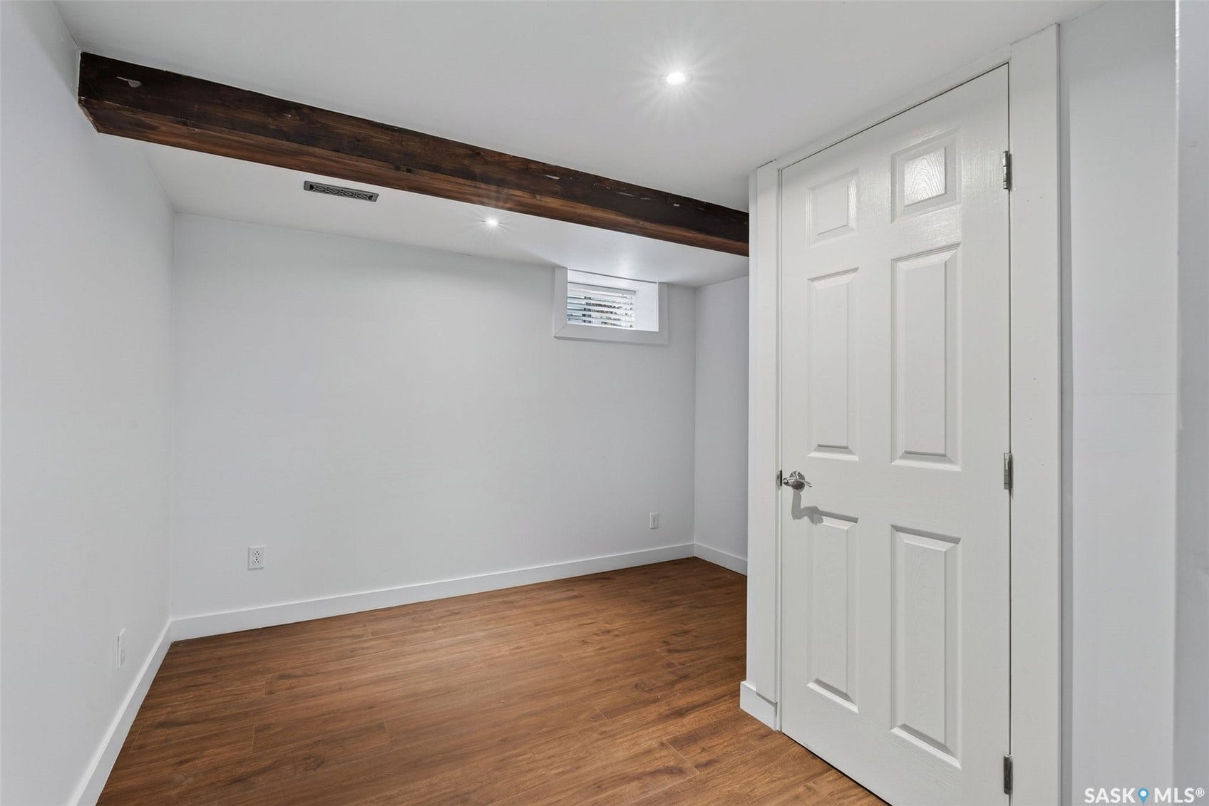 Hardwood-finish flooring with white baseboards, a white six-panel door with chrome hardware, and recessed ceiling lighting