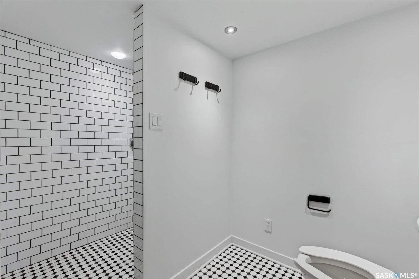 Walk-in shower with white subway tile, black and white hexagonal floor tiling, and recessed lighting
