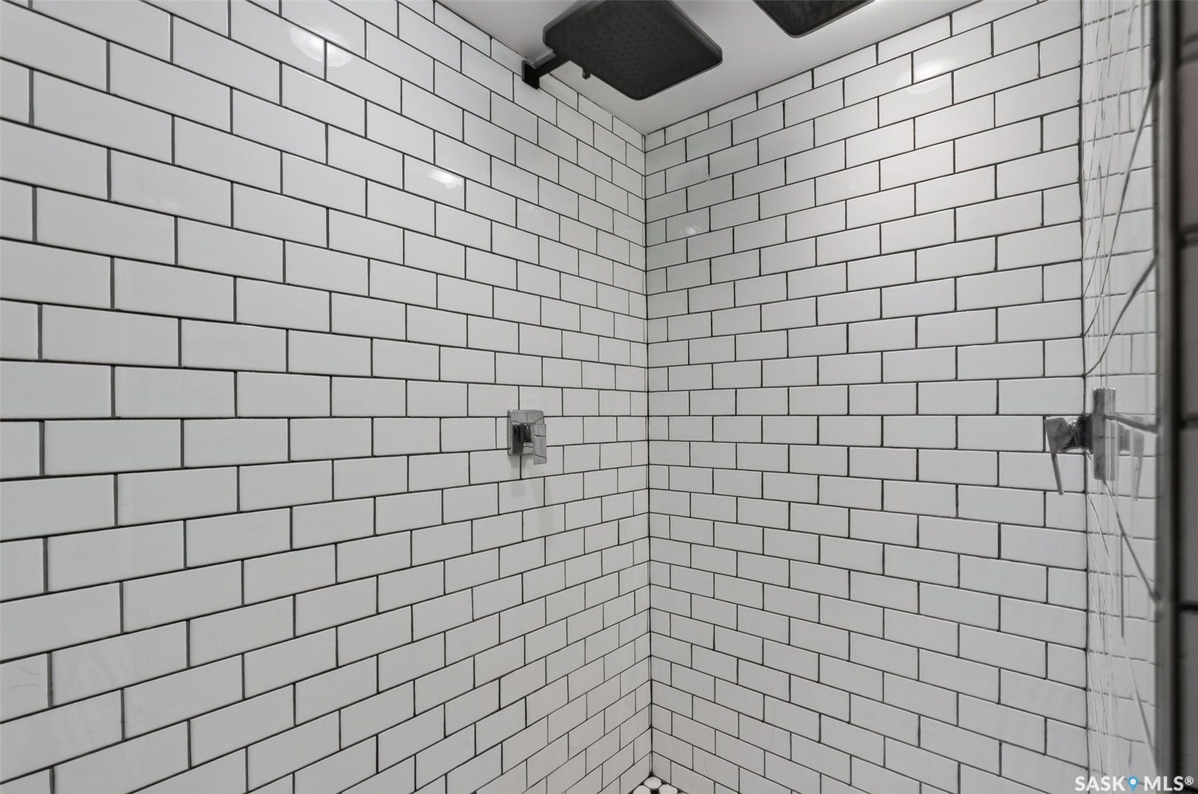 White subway tile walls with dark grout, a square rain showerhead, and a wall-mounted shower control