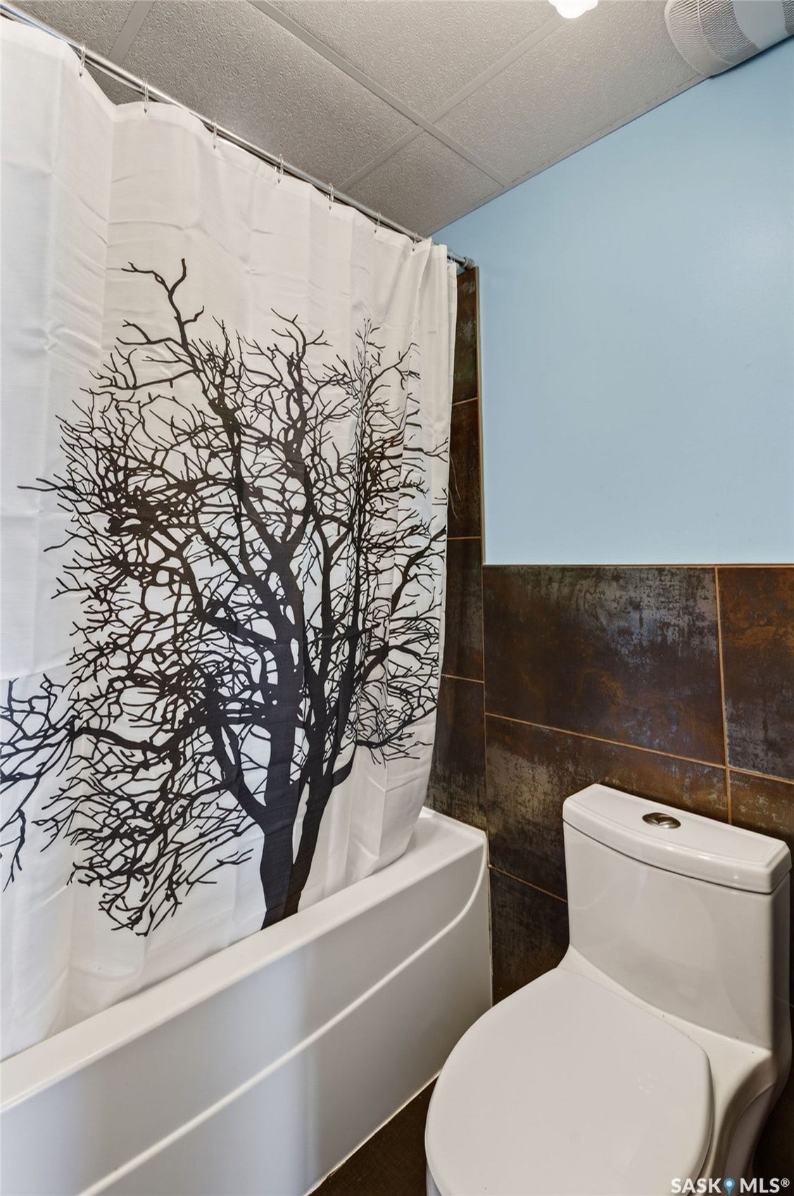 White porcelain bathtub, dual-flush toilet, and brown-toned wall tiling