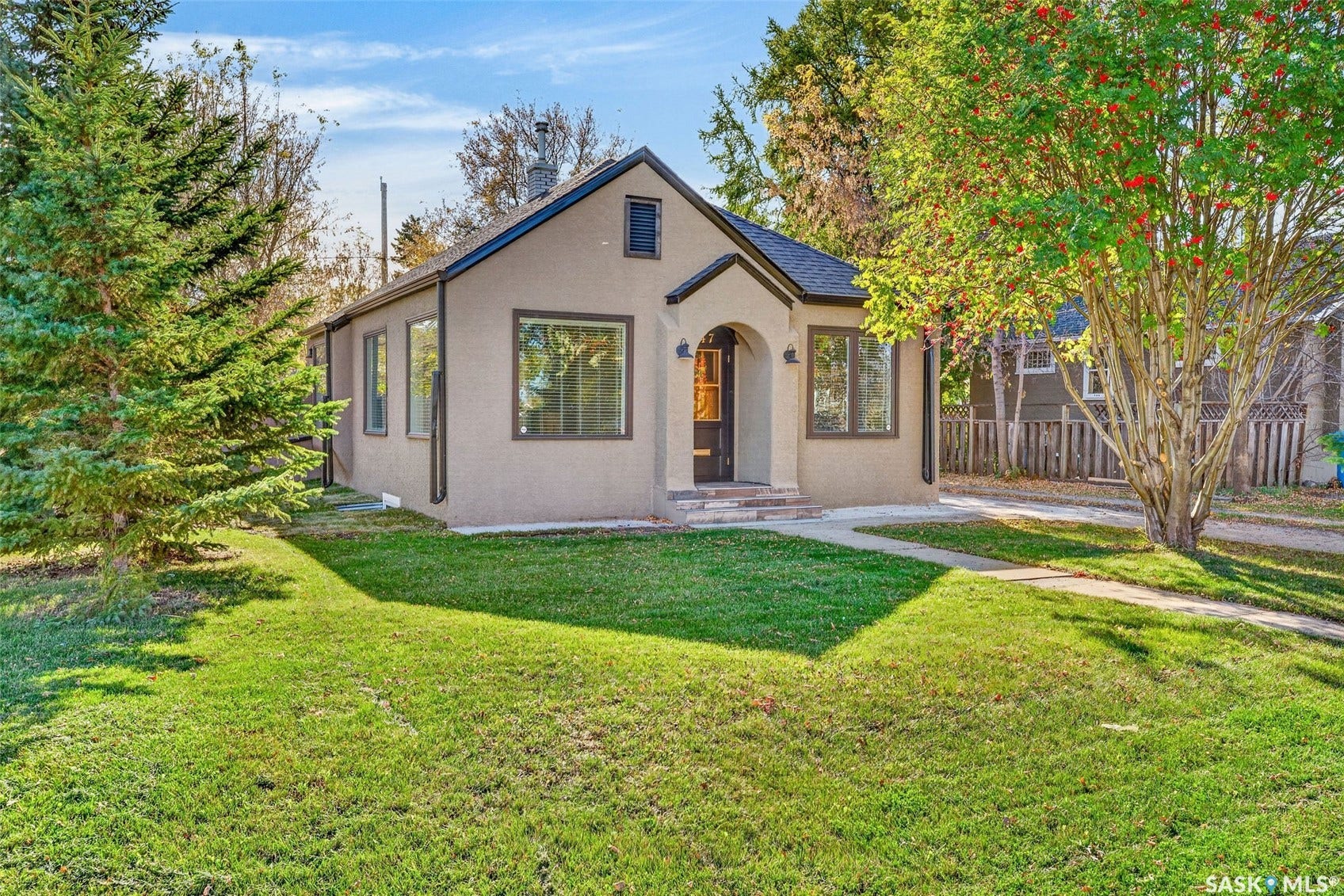 Stucco exterior with dark trim windows, arched entryway, and mature trees framing the property