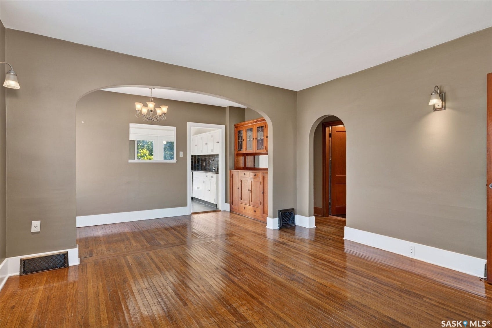 Hardwood flooring, arched doorways, built-in cabinetry, and wall sconce lighting