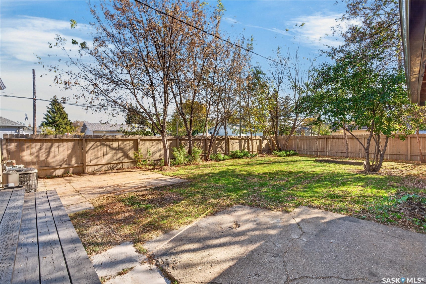 Expansive backyard featuring a wood privacy fence, mature trees, a wood deck, a concrete patio, and a grass lawn