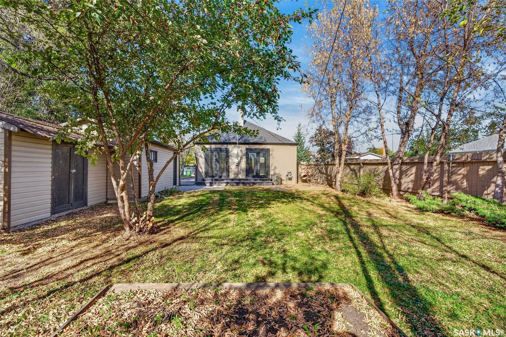 Expansive green space with mature trees, a detached storage shed, and a privacy fence