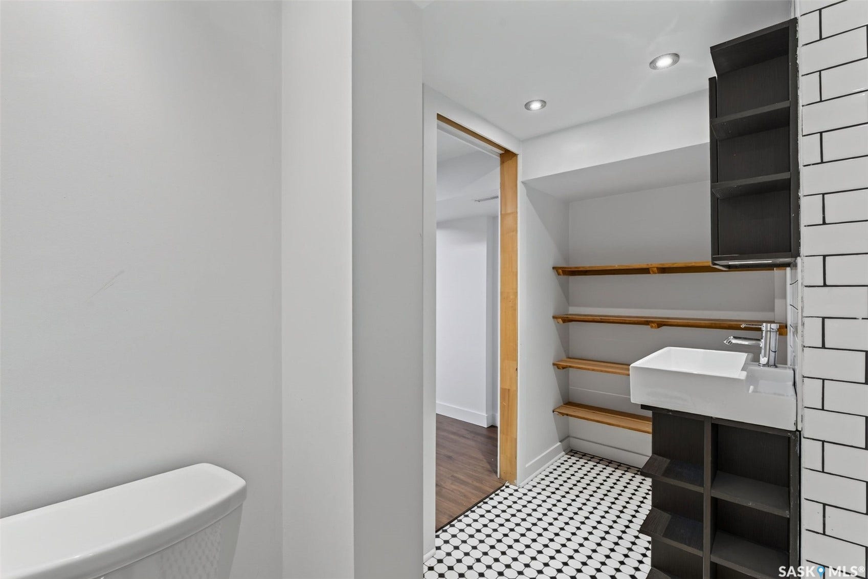 Black and white hexagonal floor tiling, wall-mounted white subway tile, a vessel sink with a chrome faucet, custom built-in shelving, and recessed lighting