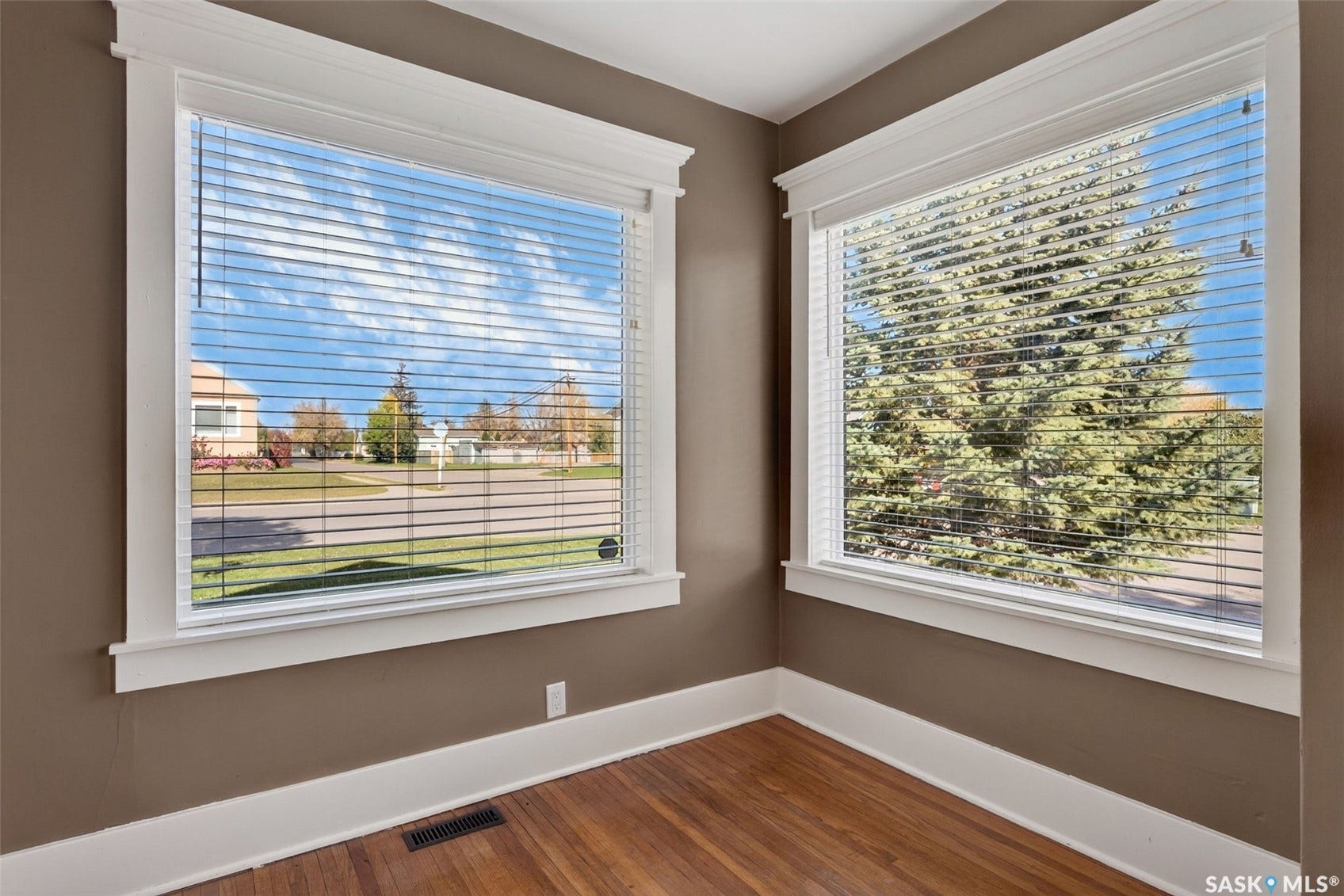 Hardwood flooring, two windows with blinds, and painted walls with white trim