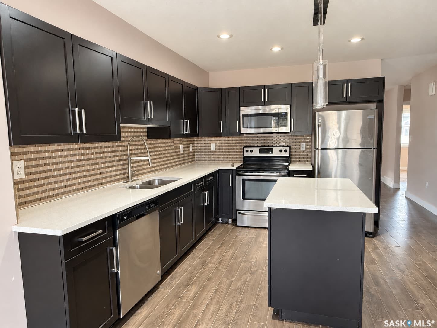 Modern kitchen featuring dark cabinetry, stainless steel appliances, a mosaic tile backsplash, and light countertops