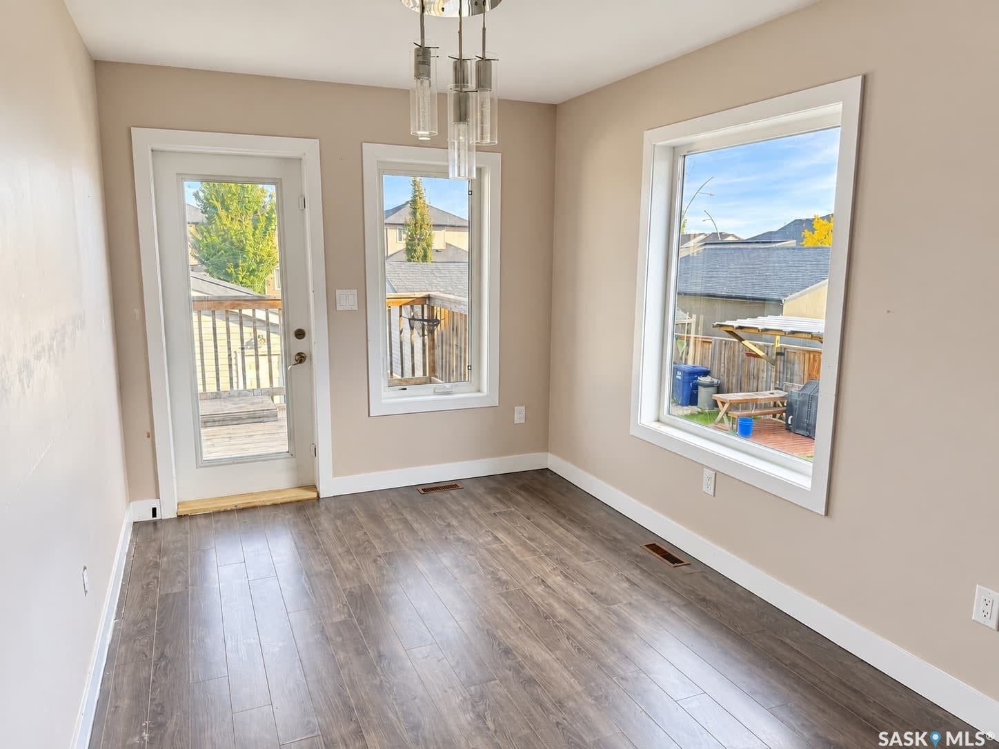 Wood-finish flooring, multiple windows, a glass-paneled door leading to an exterior deck, and a contemporary ceiling light fixture