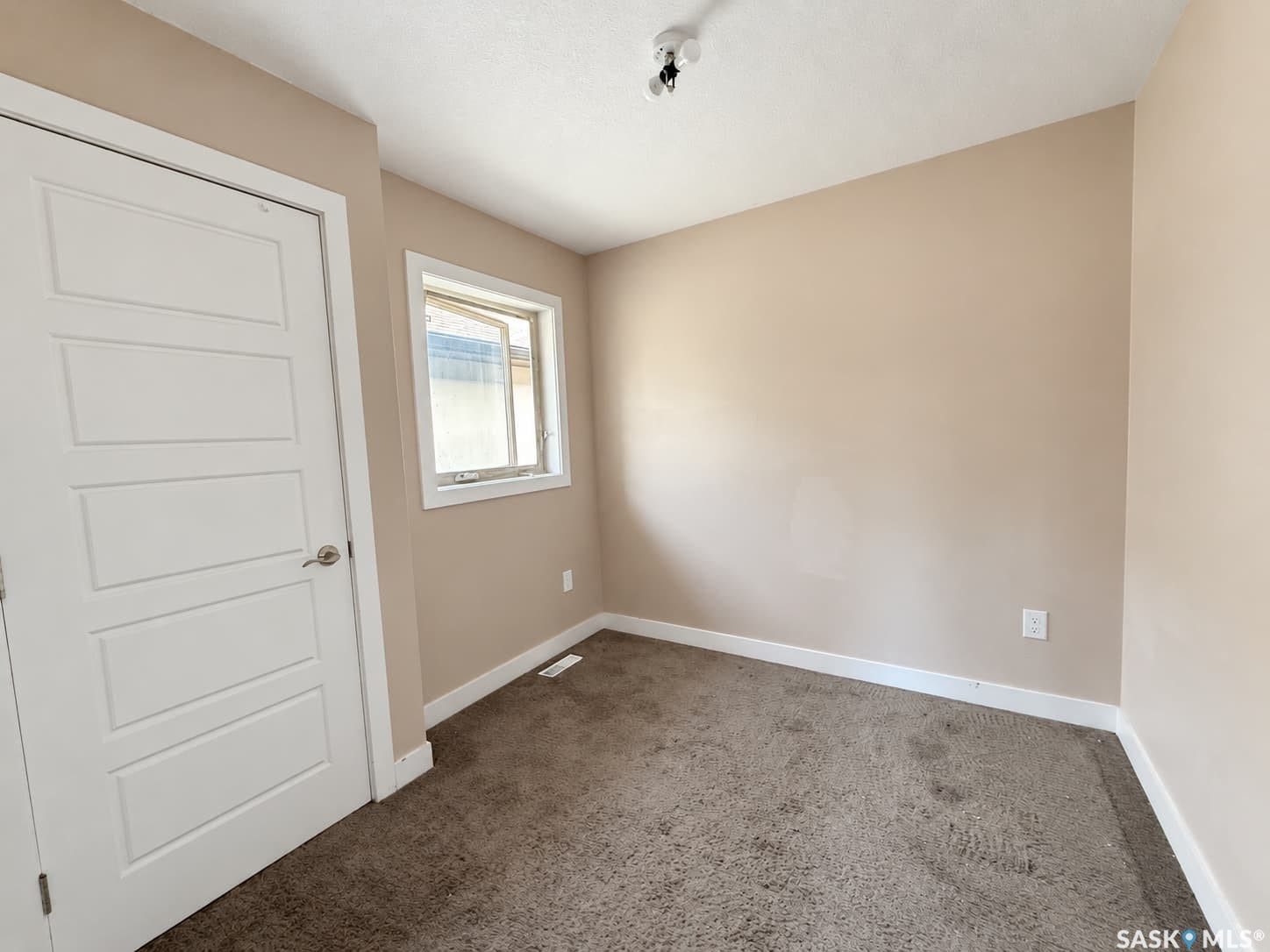 Neutral-toned walls, plush carpeting, a single window, a flush-mount ceiling light, and a white panel door