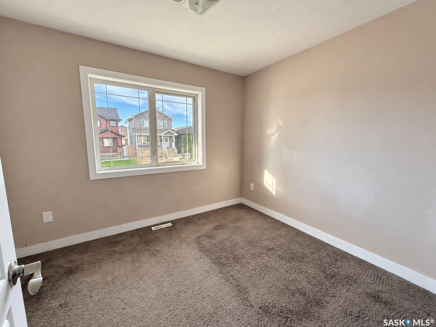 Bright interior space featuring a window with white trim, tan wall finishes, and brown carpeting
