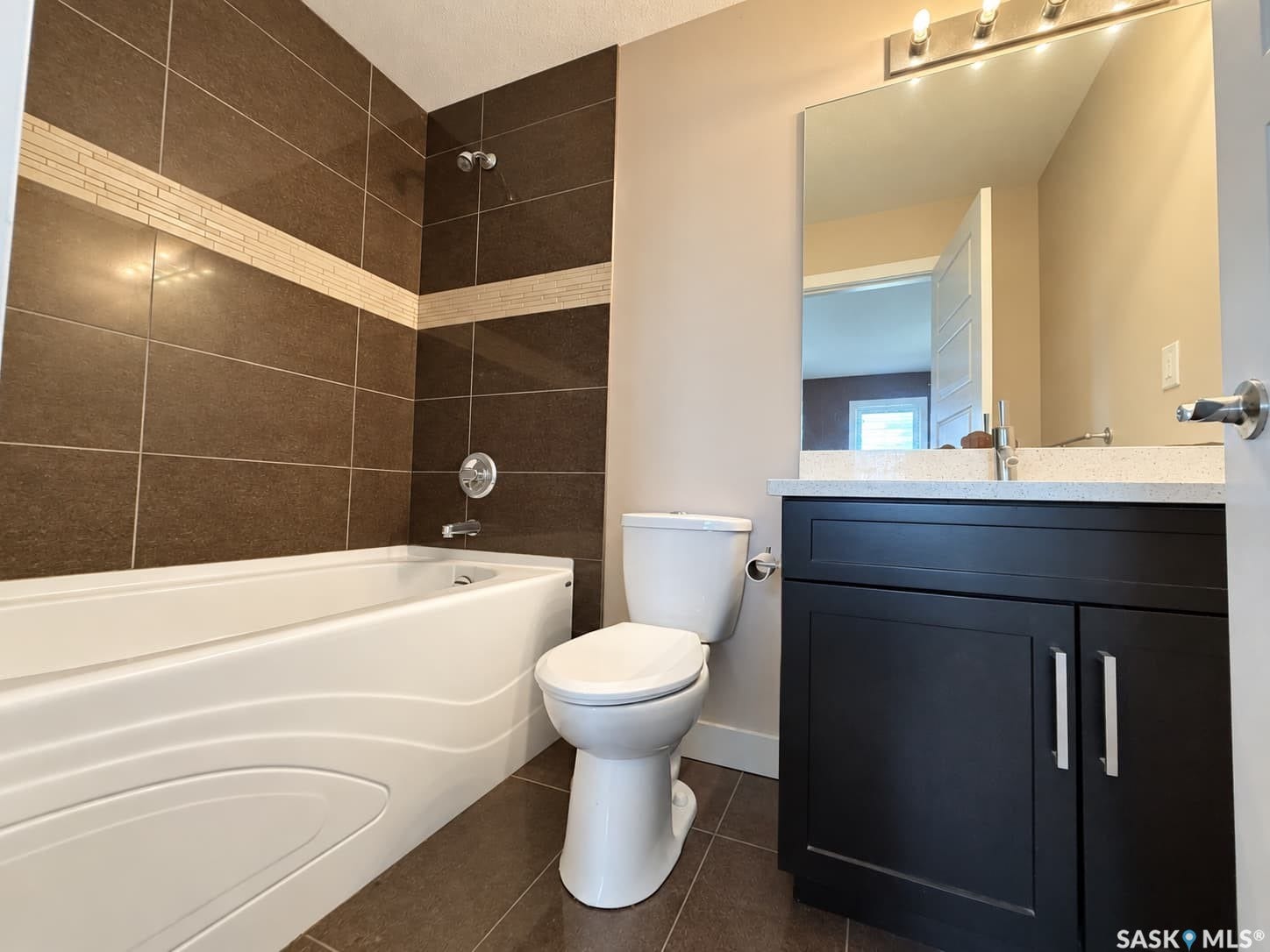 Bathtub with tiled surround, dark wood-finish vanity with a light countertop, and a large wall-mounted mirror