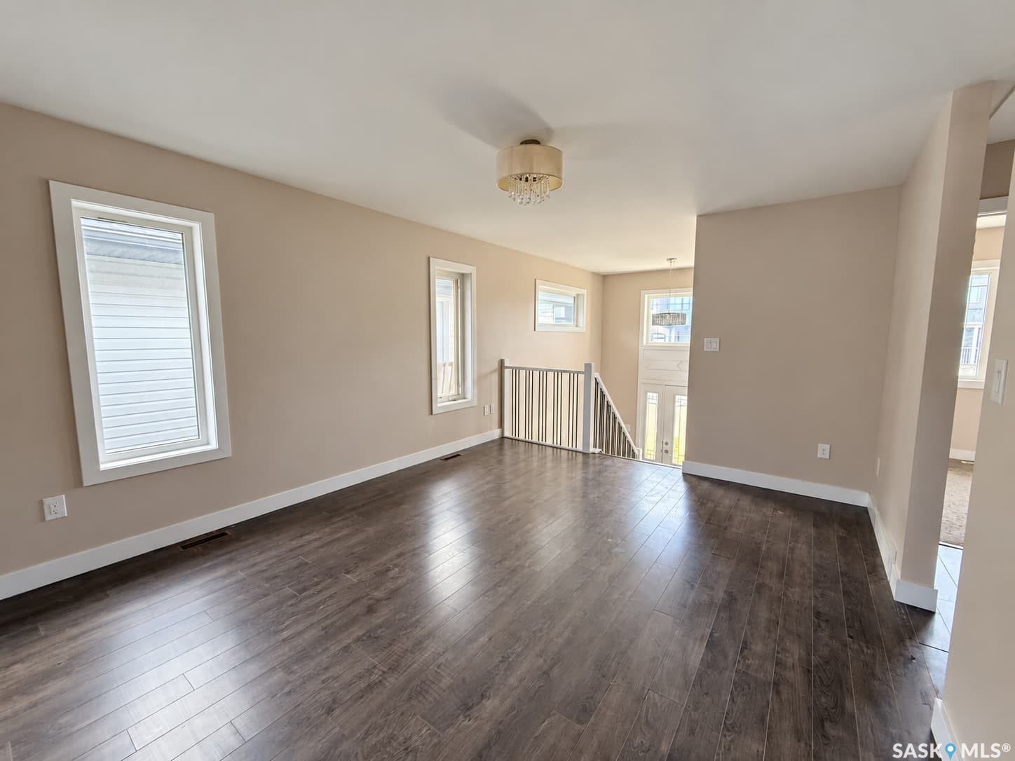 Wood-finish flooring throughout, multiple windows with white blinds, and a staircase with a white railing