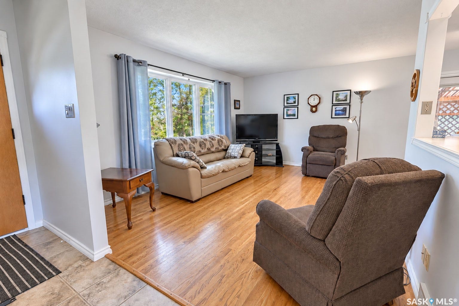 Bright living area featuring wood-finish flooring, a large bay window, and a pass-through opening to an additional space