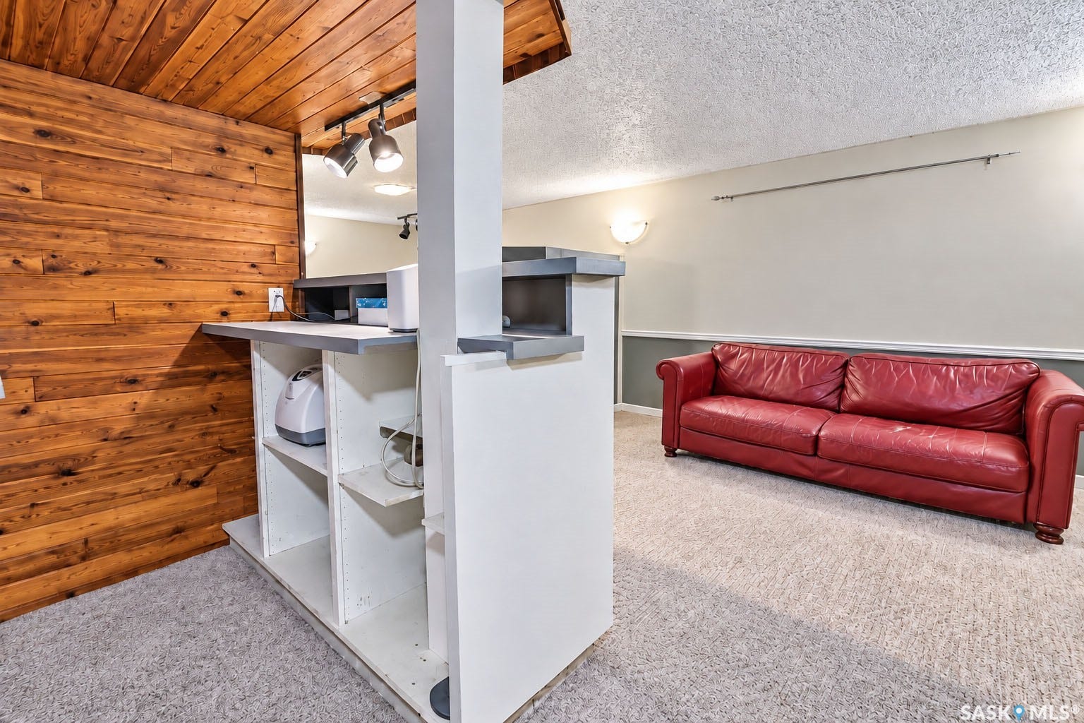 Warm wood paneling, built-in shelving, track lighting, wall-mounted sconce, and textured carpeting