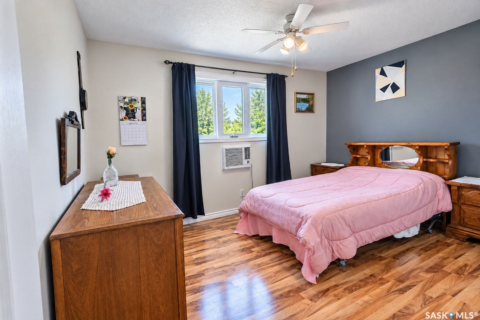 Wood-finish flooring, ceiling fan, window with dark drapes, light gray wall, and a contrasting dark gray accent wall
