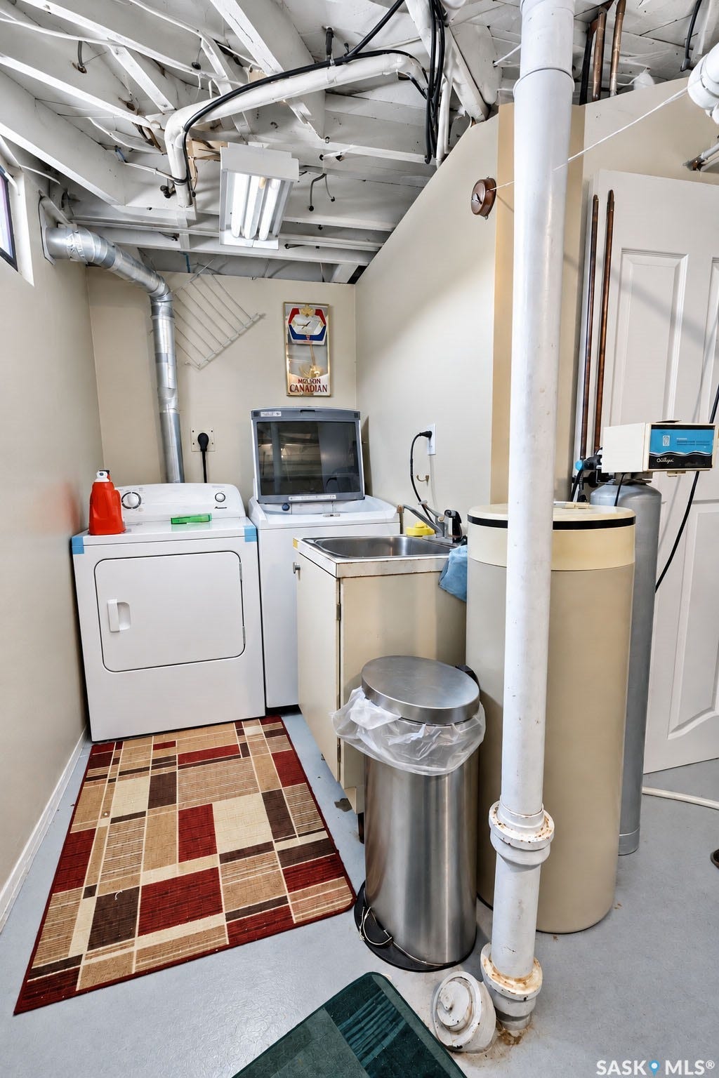 Utility area featuring exposed ceiling joists, light-colored walls, a utility sink, and visible plumbing