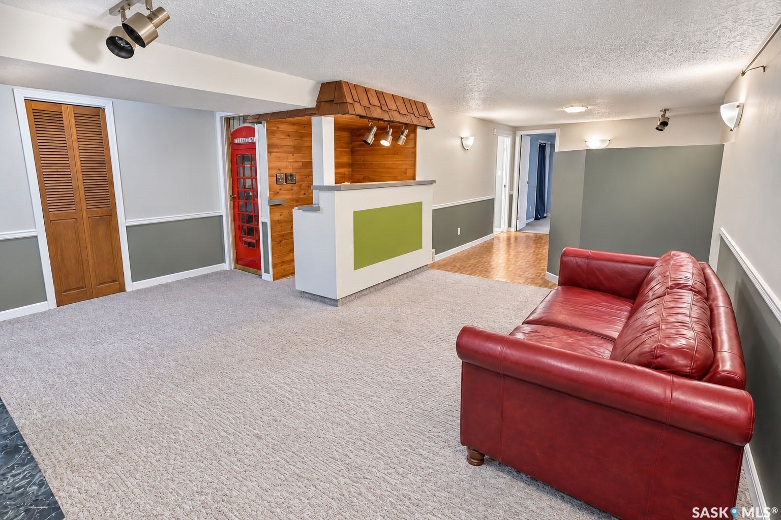 Carpeted flooring extending to wood-finish flooring, accent wall paneling, track lighting, and wall sconces