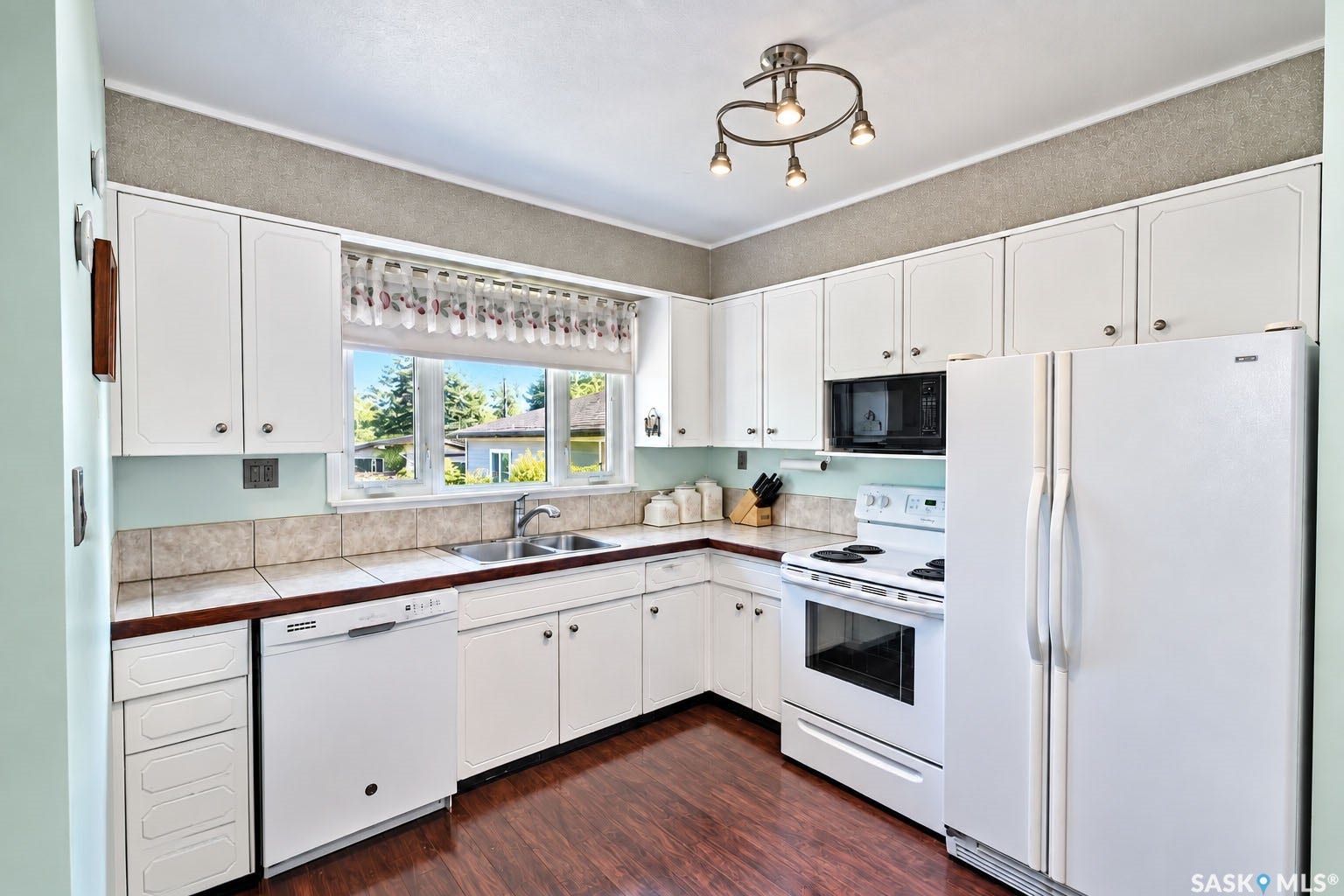 White cabinetry, wood-finish flooring, tile backsplash, stainless steel double basin sink, and recessed lighting