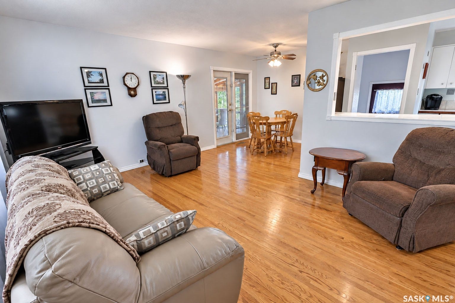 Hardwood flooring, light gray wall paint, doorway with exterior light visibility, interior pass-through window, ceiling fan with light fixture