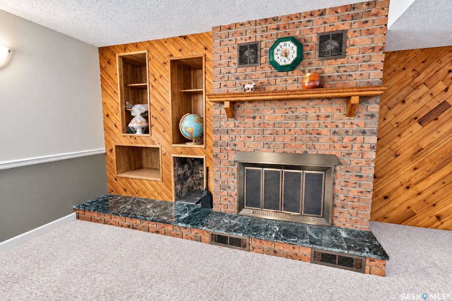 Brick fireplace with a brass-finish insert, wood mantel, built-in shelving, and a dark stone hearth