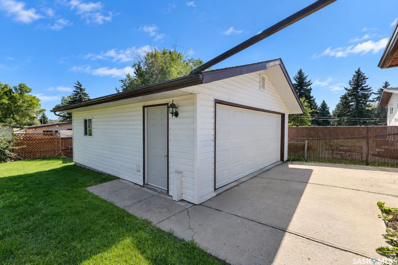 Detached garage featuring white siding, a segmented garage door, and a dedicated entry door