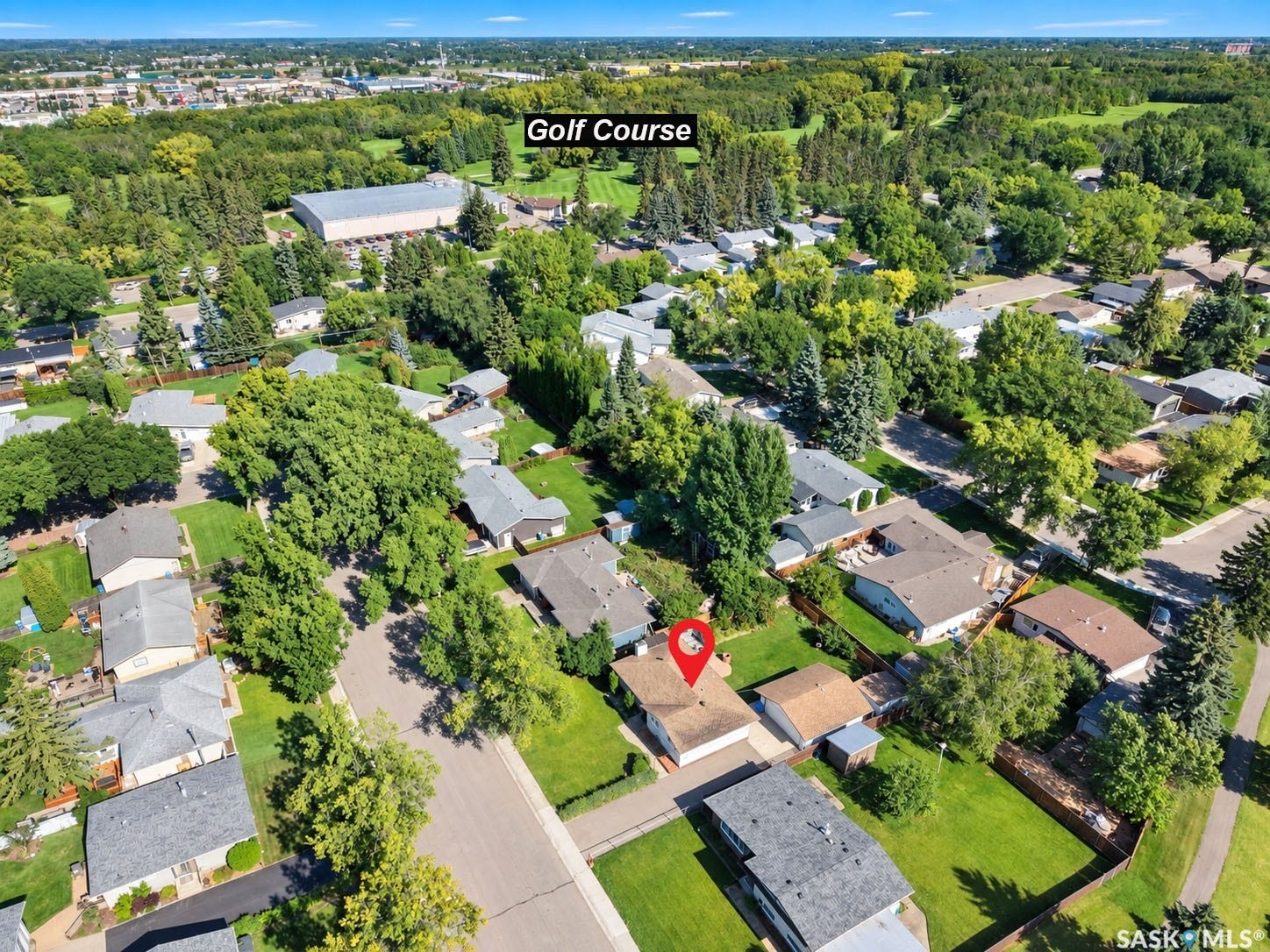 Aerial perspective of a residential neighborhood with a golf course in the background, featuring mature trees and expansive green spaces