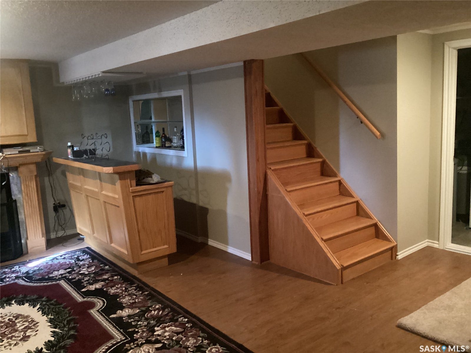 Wood-finish flooring, built-in wooden bar, wooden staircase with railing, recessed window feature, and sliding glass door