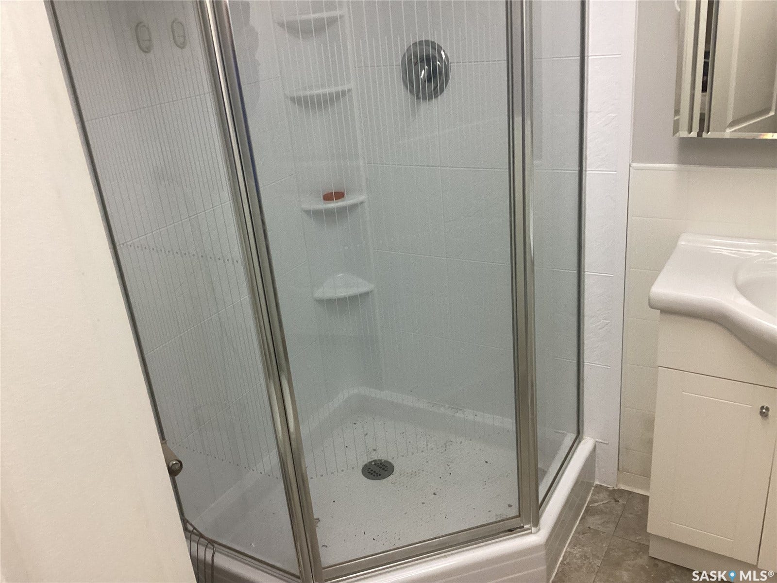 Corner shower enclosure with glass panels, white tile surround, and built-in shelves